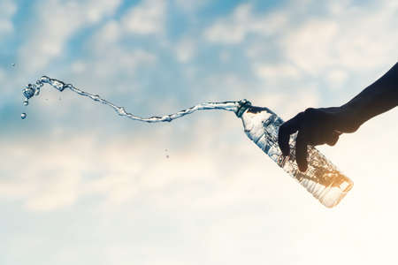 Man pour water splashing from bottle on sunset sky and cloudy abstract background.の写真素材