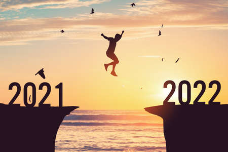 Silhouette man jumping between cliff with number 2021 to 2022 and birds flying at tropical sunset...
