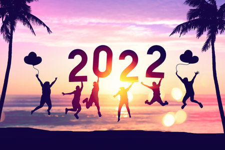 Silhouette friends jumping and holding number 2022 on sunset sky with palm tree abstract background at tropical beach. Happy new year and holiday celebration concept. Vintage tone color style.の写真素材