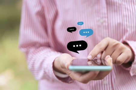 Close up woman hand hold using smart phone with chat icon flying at outdoor nature park background....