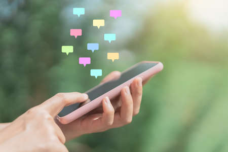 Close up woman hand hold using smart phone with chat icon flying at outdoor nature park background. Copy space of technology business and travel holiday concept. Vintage tone filter effect color.の写真素材