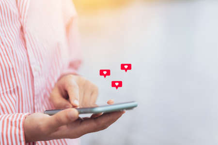 Close up woman hand hold using smart phone with heart icon at outdoor park street background. Copy...