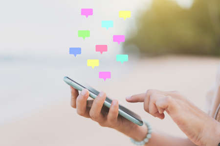 Woman hand using smart phone with message chat icon flying on tropical beach abstract background....