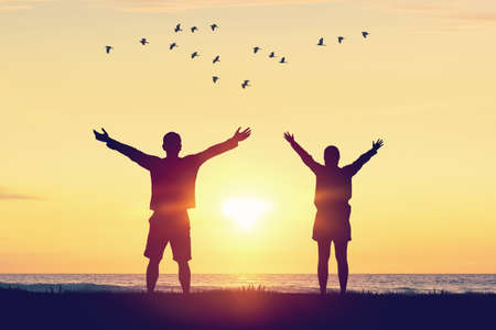 Couple raise hand up on sunset sky at beach and island with birds flying abstract background....