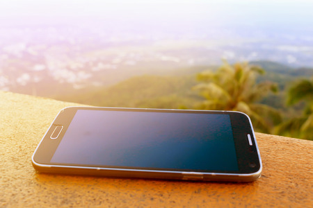 Mobile Phone on wood, City and mountain Background.