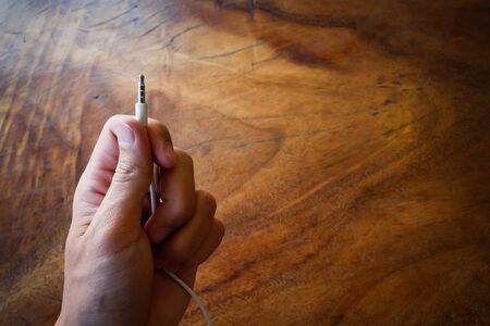 Hand holding Socket from white in ear headphones on Wood background.