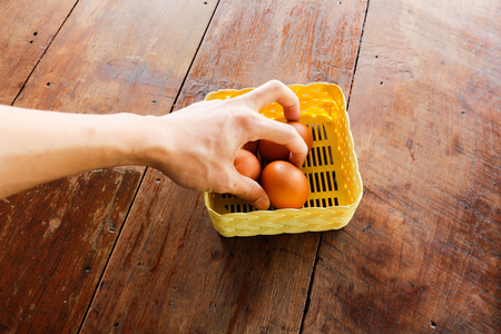 A man's hand picking egg from egg rattan basket. On old wooden table.の写真素材