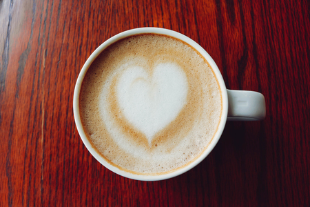 Latte coffee on coffee shop with heart pattern in a white cup on wooden table backgroundの写真素材