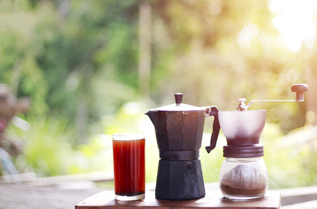 Freshly ground coffee beans in coffee grinder and hot coffee on a cup on wood table in the morningの写真素材