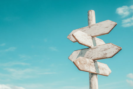 Rustic wooden signpost against a clear blue sky, indicating different directions for exploration and adventure in a serene outdoor setting.の素材