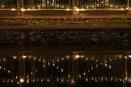 Decorated bulbs hanged on wall with reflections of canal at night