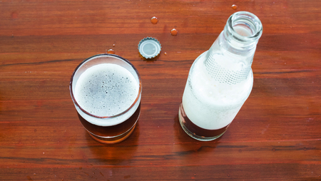 Glass and bottle of beer with openned bottle cap on wooden tables