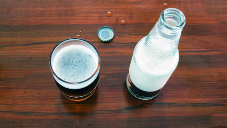 Glass and bottle of beer with openned bottle cap on wooden tablesの写真素材
