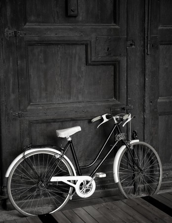 Aged vintage black bicycle, big wooden door, black and whiteの写真素材