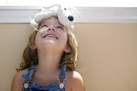 Happy toddler blond girl with toy dog over headの写真素材