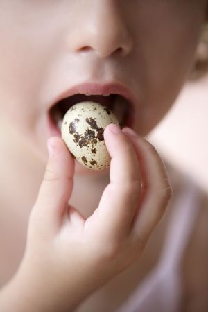 Little girl holding quail egg pretending to eat