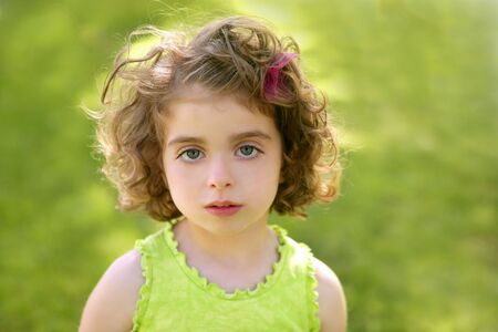 Beautiful brunette blue eyes little girl portrait on the park green grassの写真素材