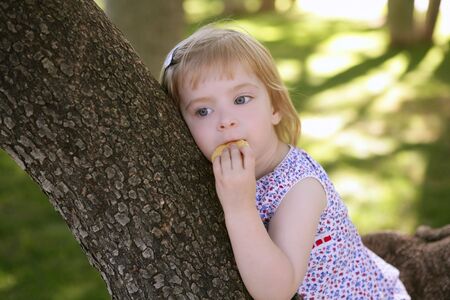 Beautiful little girl eating biscuit over the green park treeの写真素材