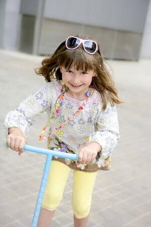 Brunette little girl with scooter in gray city backgroundの写真素材