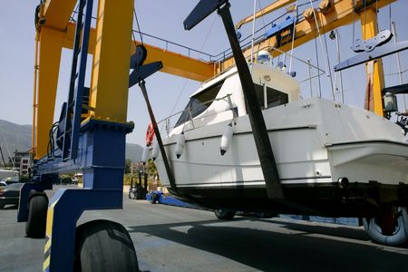Dock crane elevating a fishing boat in Mediterranean marinaの写真素材
