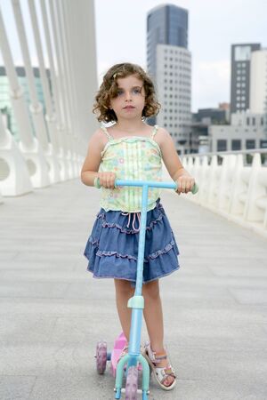 Brunette little girl with scooter in gray city backgroundの写真素材