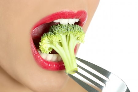 Broccoli on steel fork in woman mouth with red lipsの写真素材