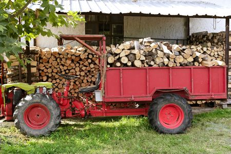 Firewood working tractor in red color with stacked woodの写真素材