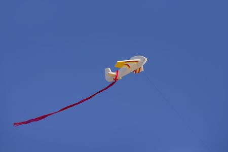 Airplane kite flying on blue sunny sky with red tailの写真素材