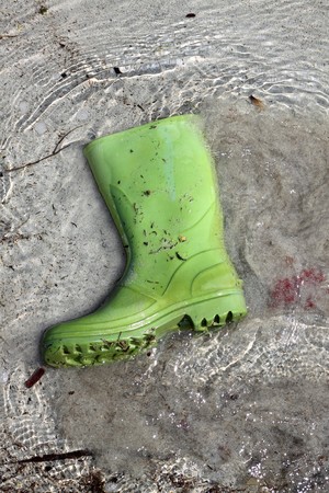 green boots trash on beach shore pollution human waste concept