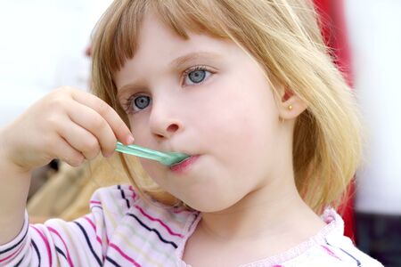blond little girl eating ice cream color spoon portraitの写真素材