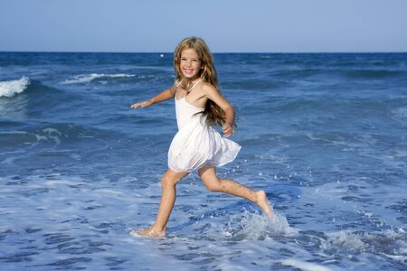 Little girl running beach shore splashing water in blue seaの写真素材