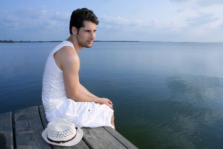 Mediterranean young latin man relaxed on wood pier white hatの写真素材
