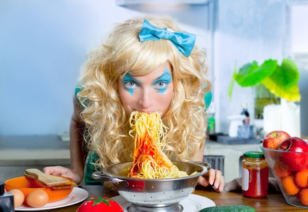 Blonde funny girl on kitchen eating pasta like crazy with blue makeupの写真素材