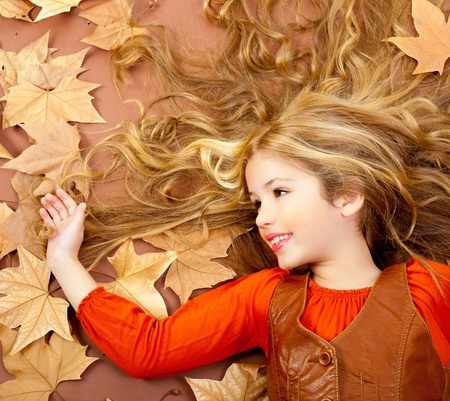 autumn fall little blond girl on dried tree leaves background and long spread hairの写真素材