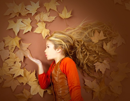 autumn fall little blond girl on dried tree leaves blowing wind with lipsの写真素材