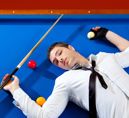 billiard young man player lying on pool blue table with ballsの写真素材