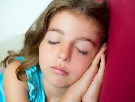 beautiful brunete kid girl sleeping hands together on red sofaの写真素材