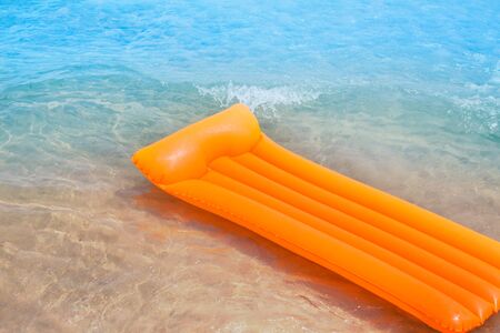 Beach shore with orange floating lounge and waves over sand bottomの写真素材