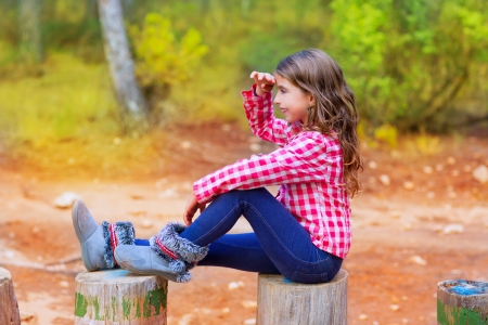 Kid girl sitting in forest trunk looking far away with hand in foreheadの写真素材