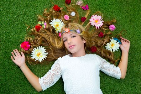 Blond spring children girl with flowers on hair over green grass floorの写真素材