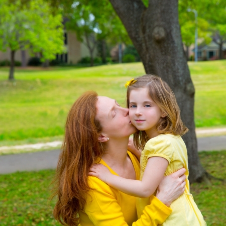 Mother kissing her blond daughter in green park outdoor dressed in yellowの写真素材