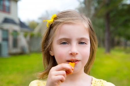 Blond kid girl eating corn snacks in outdoor park in lawn backgroundの写真素材