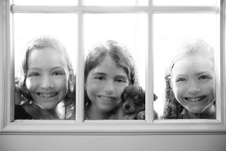 three sister friends looking through the window with a pup and raindropsの写真素材
