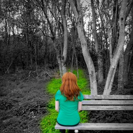Lonely redhead woman rear view looking to forest sitting on a park benchの写真素材