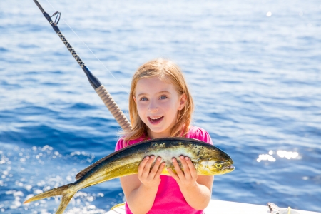 Blond kid girl fishing Dorado Mahi-mahi fish happy with trolling catch on boat deckの写真素材