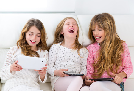 three kid sister friends girls group playing together with tablet pc on white sofaの写真素材