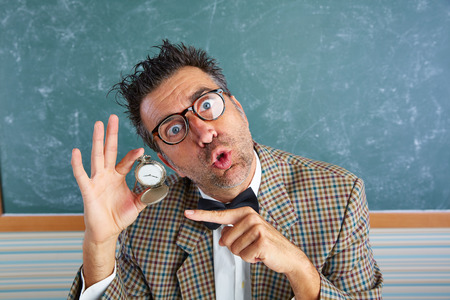 Nerd silly teacher showing vintage chain watch in green blackboardの写真素材