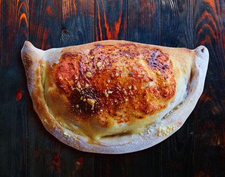 Pizza Calzone folded as a patty on a wooden board table