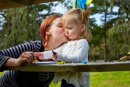 Mother kissing daughter drawing colors in a park lakeの写真素材