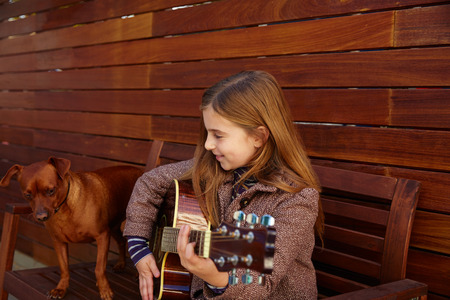 blond kid girl playing guitar with dog and winter beret on wooden backgroundの写真素材
